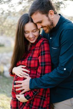Smiling man hugs a pregnant woman from behind. Close-up. High quality photo