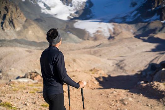 A young man travels, goes to the mountains in thermal underwear and with trekking poles, a hiker climbs to the top of the mountain, against the backdrop of red rocks and a glacier.