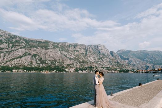 Groom and bride hug on the pier against the background of the sea and mountains. High quality photo