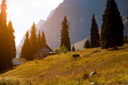 Beautiful landscape with cozy modern house among high mountains and green meadows at sunset.