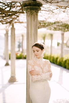 Bride in a dress stands near a column in an old patio. Portrait. High quality photo