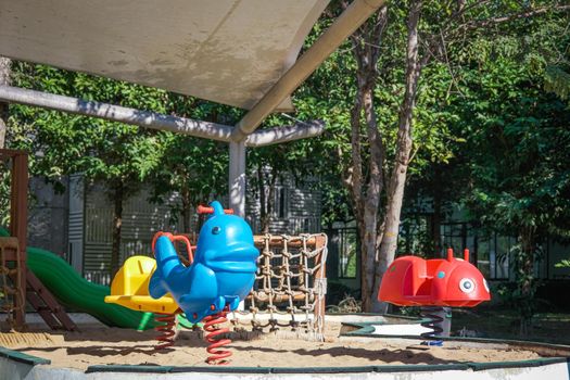 Colorful playground on yard in the park. Rocking horse and climbing rope for children in public park.