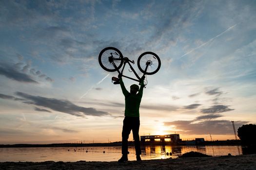 The cyclist rejoices at the victory on the shore of the lake. Dark foreground