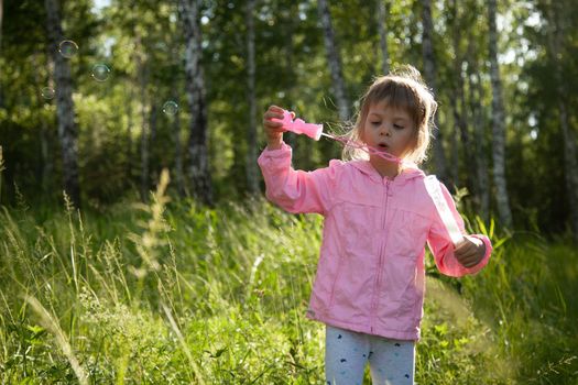 Little girl blowing soap bubbles in the forest. Happy child