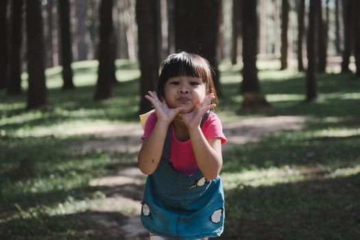 Active little girls running in the pine forest on a warm summer day. Happy girl smiles and laughs while spending time with her family in the park on vacation.