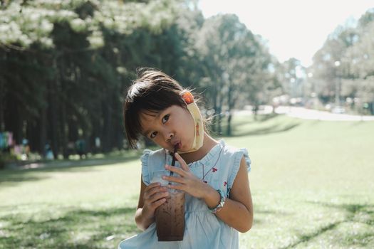 Cute little girl drinking delicious iced chocolate or cocoa in the summer outdoor garden. Family having a picnic in the park.