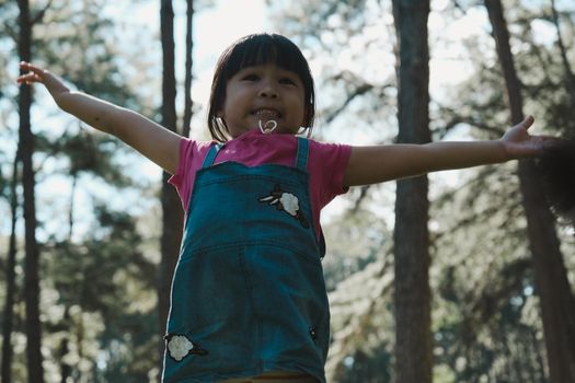 Active little girls running in the pine forest on a warm summer day. Happy girl smiles and laughs while spending time with her family in the park on vacation.