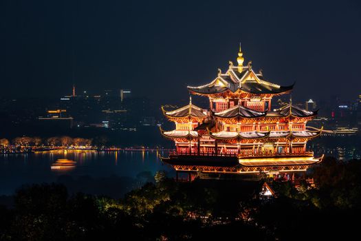 Night view of illuminated Cheng Huang Ge (City God Pavillion) with West Lake and city skyline on background, Hangzhou, China