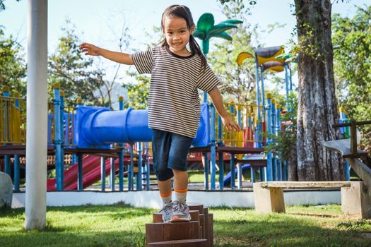 Active little girl walking on balance beam in the outdoor playground in the park. Happy child girl having fun in children playground. Play is learning in childhood.