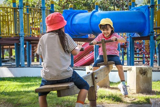 Active little sisters playing on a seesaw in the outdoor playground. Happy child girls smiling and laughing on children playground. Play is learning in childhood.