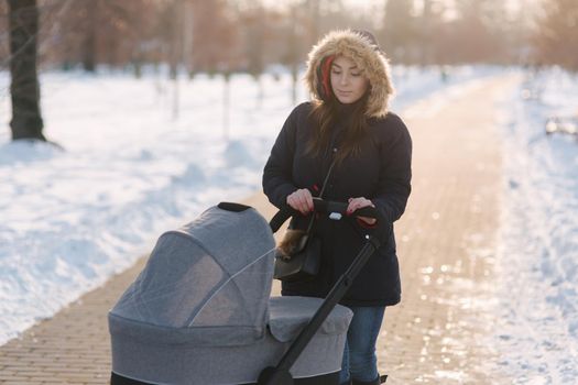 Mom walk with baby in pram. Winter park. Happy woman with her baby.