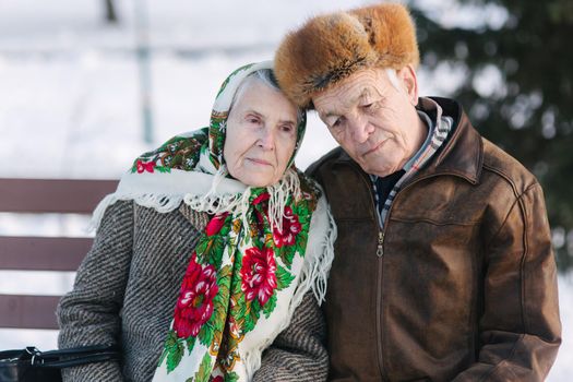 Senior people sitting on the bench in the park. Happy elderly couple spend time outside in winter.