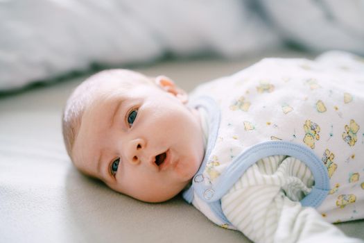 Baby lies on the bed with his head turned to the side and his mouth open. High quality photo