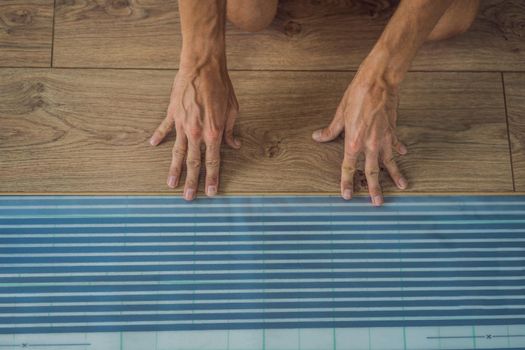 Man installing new wooden laminate flooring on a warm film floor. Infrared floor heating system under laminate floor.