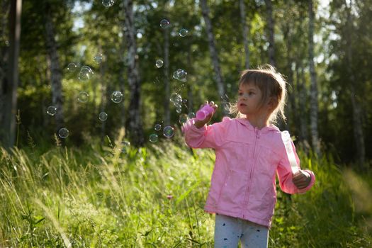 Little girl blowing soap bubbles in the forest. Happy child