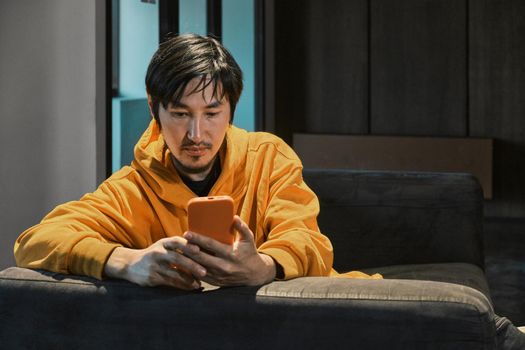 An Asian guy sits on sofa in a small office and communicates by mobile phone. The concept of small business and online communication.