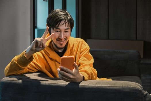 An Asian guy sits on sofa in a small office and communicates by mobile phone. The concept of small business and online communication.