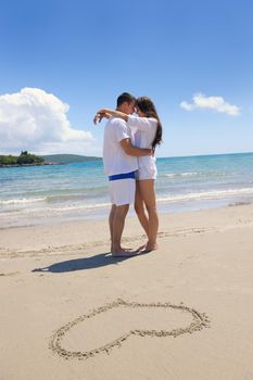 happy young couple have fun and relax  on the summer with heart drawing on beach sand