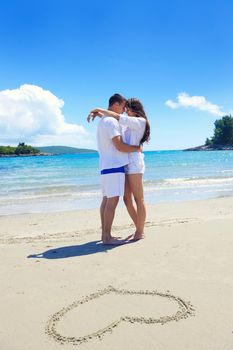 happy young couple have fun and relax  on the summer with heart drawing on beach sand