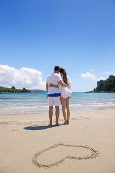 happy young couple have fun and relax  on the summer with heart drawing on beach sand