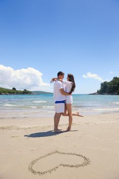 happy young couple have fun and relax  on the summer with heart drawing on beach sand