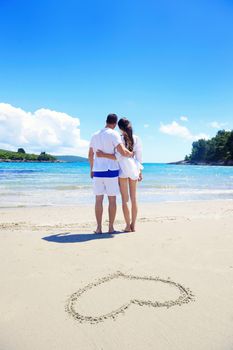 happy young couple have fun and relax  on the summer with heart drawing on beach sand