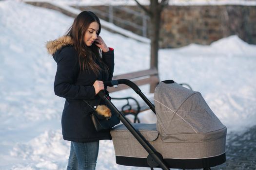 Young mother walking with her baby in pram. Beautiful stoller. Winter photosession.