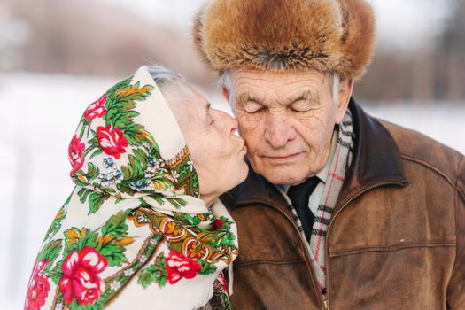 Portrait of happy senior couple. Elderly woman kiss her husband in weighty. old couple walking in the park in winter time. Happy family. Gold wedding.