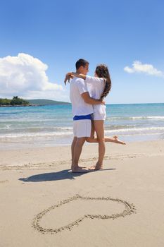 happy young couple have fun and relax  on the summer with heart drawing on beach sand