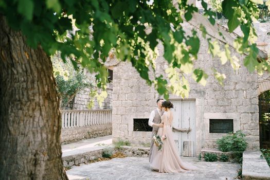 Bride and groom hugging near a stone building. High quality photo