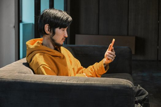 An Asian guy sits on sofa in a small office and communicates by mobile phone. The concept of small business and online communication.