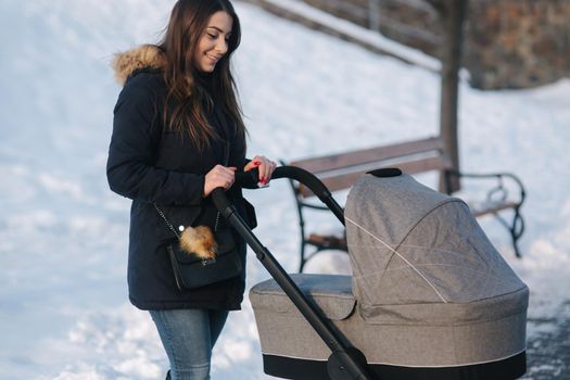 Young mother walking with her baby in pram. Beautiful stoller. Winter photosession.