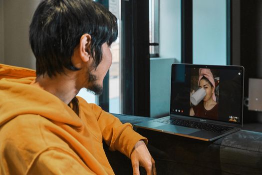 An Asian guy sits in a small office and communicates via video link through a laptop with his girlfriend. The concept of online communication, quarantine, distance.