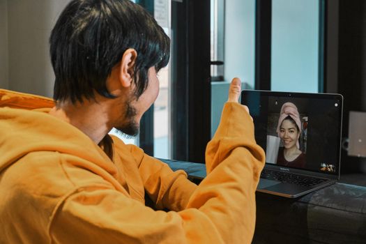 An Asian guy sits in a small office and communicates via video link through a laptop with his girlfriend. The concept of online communication, quarantine, distance.