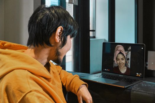 An Asian guy sits in a small office and communicates via video link through a laptop with his girlfriend. The concept of online communication, quarantine, distance.