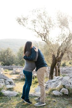 Man hugs pregnant woman standing on tiptoe in park. High quality photo