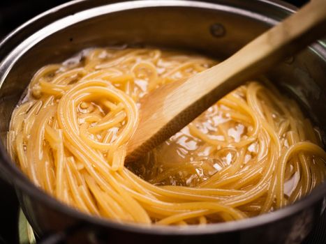 Raw spaghetti is being cooked in boiling water in a kitchen pot. Healthy Italian Food and Cooking concepts.