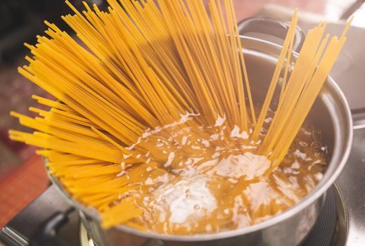 Raw spaghetti is being cooked in boiling water in a kitchen pot. Healthy Italian Food and Cooking concepts.