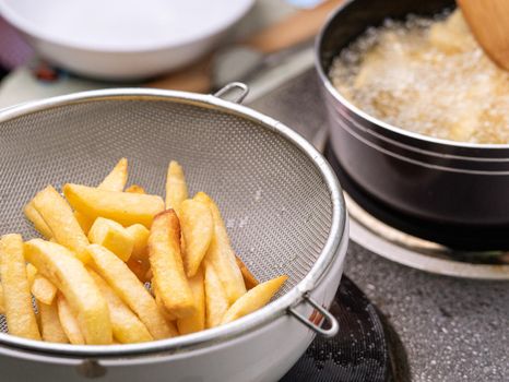Frying french fries in the fryer in hot oil on the electric stove in the kitchen and french fries in a basket to drain the oil. Making homemade french fries. selective focus
