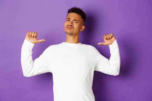 Image of confident and handsome african-american man, pointing at himself with proud face, standing self-assured over purple background.