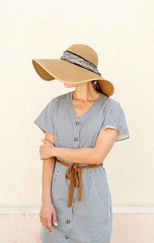 Beauty, fashion concept. Portrait of a young woman in summer straw hat on beige wall, face covered, looking away