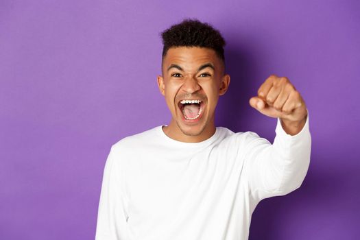 Close-up of determined and confident african-american man, raising fist and shouting black lives matter, fighting for his rights, standing over purple background.