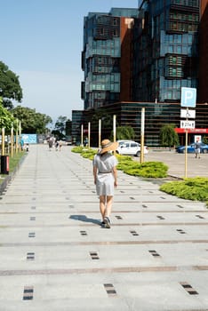 Anapa, Russia - 24 July 2021: Woman in summer dress and hat walking by the modern apartment building with green lanes, sunny summer day