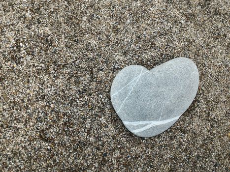 Stone heart lies in the sand. Concept of love. Copy space.