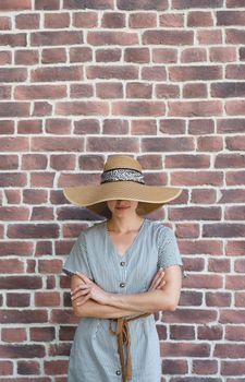 Summer style. Portrait of a beautiful young woman in summer dress and hat standing on red brick wall background