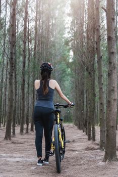 Back young female woman helmet catch bicycle at forest on summer with copy space