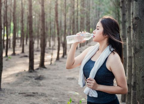 Beautiful young woman drinking water bottle after exercise fitness, in nature park forest