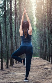 Back Beautiful young woman relaxation standing fitness exercise yoga in morning at forest tree nature park