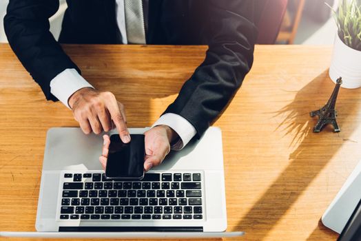 Business man using smart mobile phone with laptop computer on desk office home