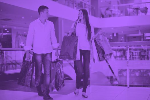 happy young couple with bags in shopping centre mall duo tone